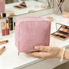 A pink ribbed storage pouch for cosmetics and sanitary napkins is held in a hand on a white surface.