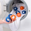 A hand is holding several reusable laundry balls for pet hair and lint removal inside a white washing machine drum.