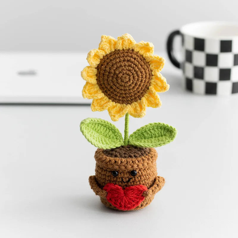 Handmade crochet sunflower doll with green leaves and a brown body sitting on a white surface.