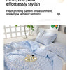 A light blue quilted blanket with a floral print is displayed on a bed, featuring a two-tone design.