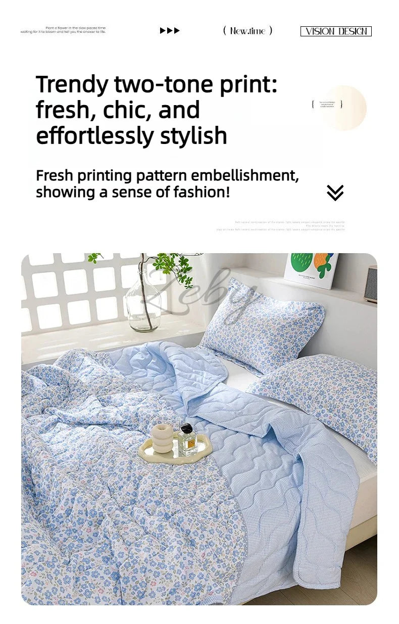 A light blue quilted blanket with a floral print is displayed on a bed, featuring a two-tone design.