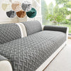 A gray quilted anti-slip sofa cushion displayed on a white sofa with decorative fabric swatches.