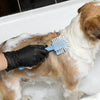 A dog is being bathed with soap and a blue brush while wearing black disposable nitrile gloves.