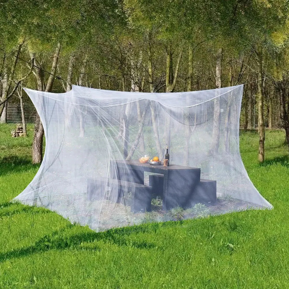 A large mesh fly net canopy is set up on the ground, featuring a dark wooden table and some items inside.