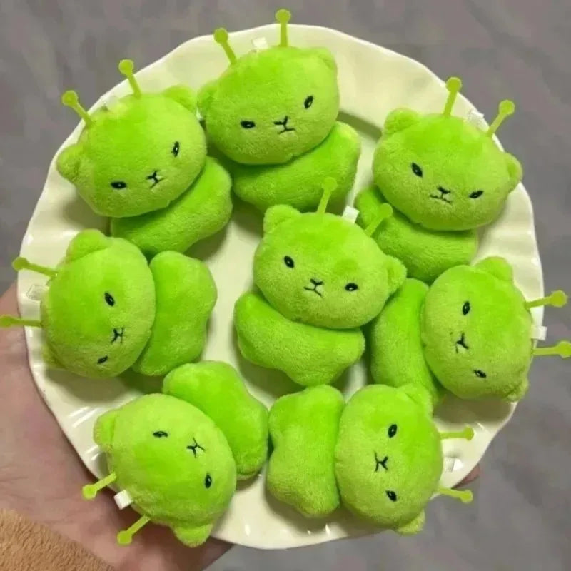 A plate of cute green alien plush keychains with small antennae arranged on a white dish.