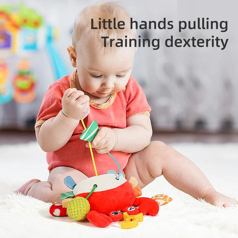 A baby is playing with a red and yellow sensory toy shaped like a crab, which has a rattle and teether.