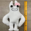 A white plush toy resembling a bird with large eyes and a pink bow.