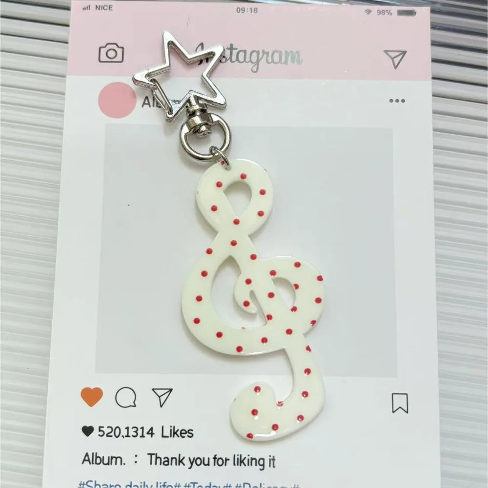 Clé portkey en acrylique transparent avec un charm étoile et une note de musique à points rouges.