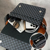 A black patterned crossbody bag is shown resting on a wooden stand, with a smartphone and sunglasses inside.