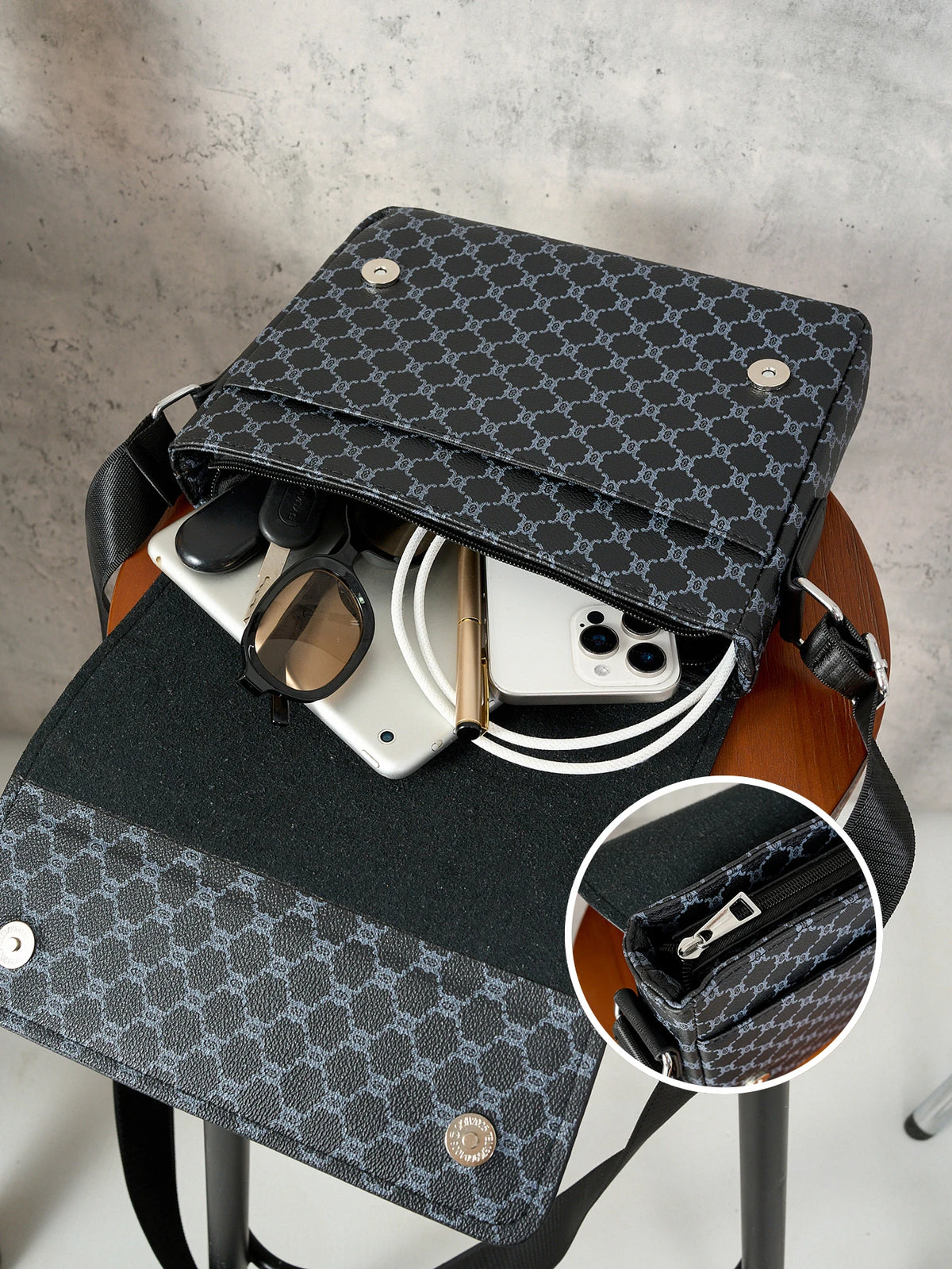 A black patterned crossbody bag is shown resting on a wooden stand, with a smartphone and sunglasses inside.