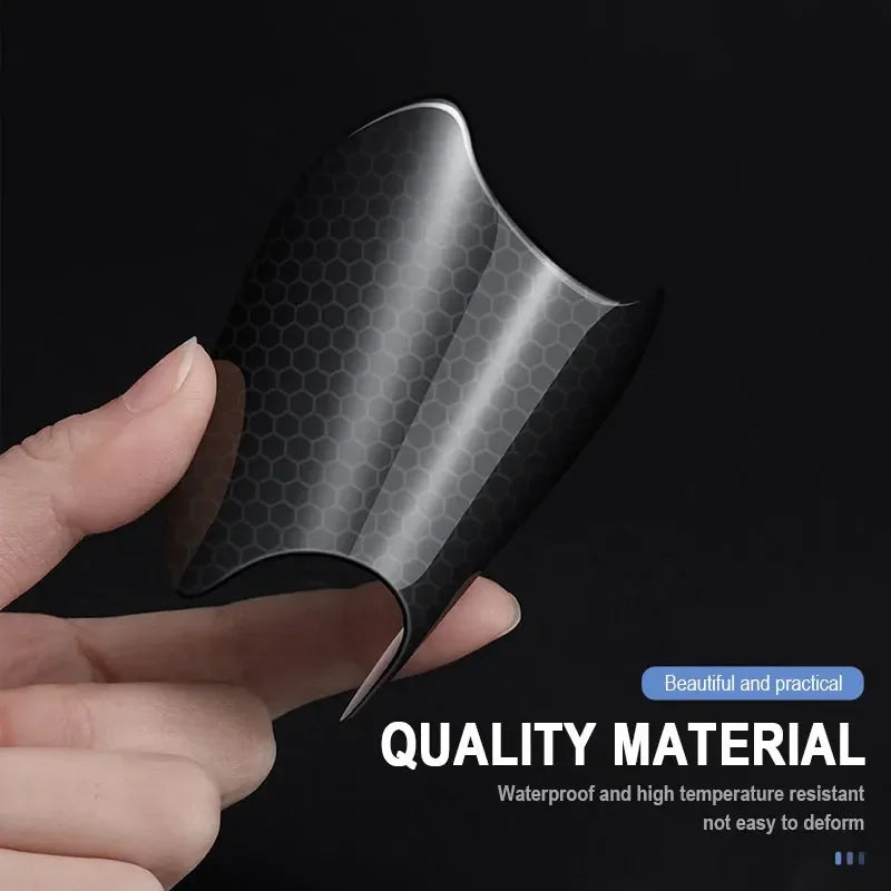 A hand holds a black carbon fiber door handle protector sticker, showcasing its texture and protective design.