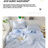 A light blue quilted blanket with a white floral pattern is displayed on a bed.