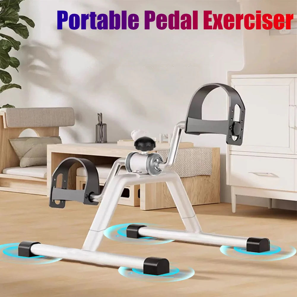 A portable pedal exerciser with a silver frame and black grips is shown on a wooden desk surface.