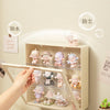 A hand places collectible dolls into a wall-mounted dustproof display case with protective labels.