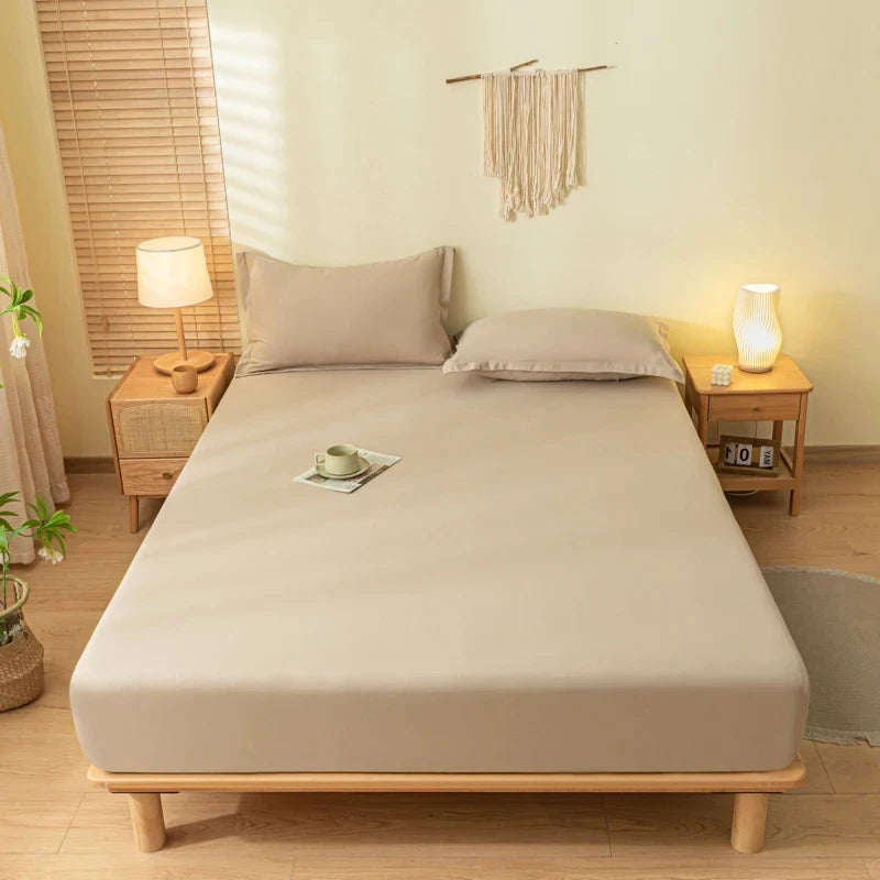 A light beige fitted bed sheet set with pillowcases is displayed on a wooden bed frame in a bright room.