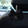 A black bow-shaped hook is attached to a car seat back, featuring a metallic accent.