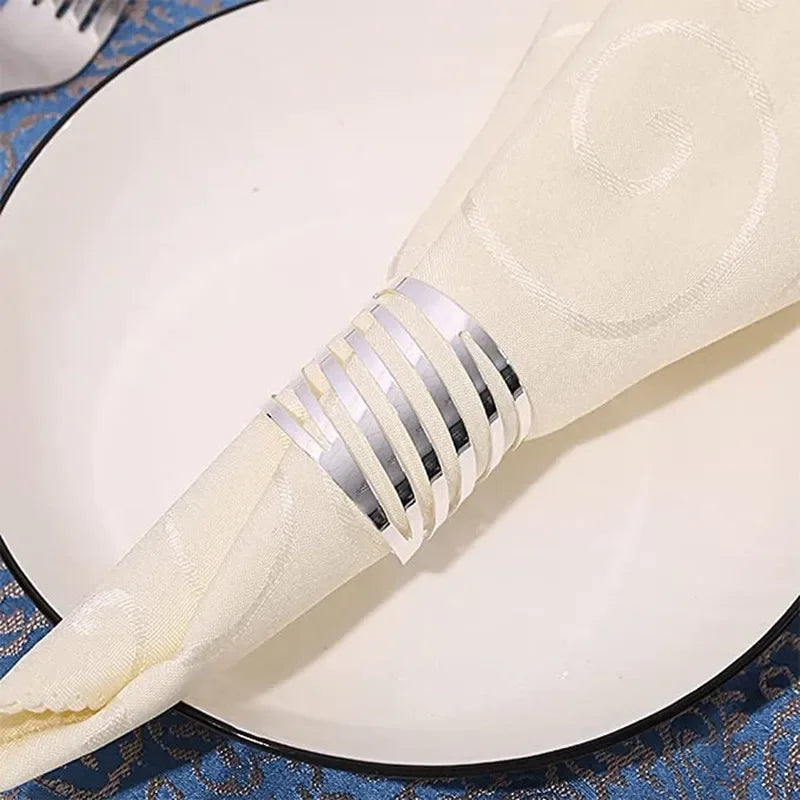 A set of twelve decorative metal napkin rings with a hollow-out pattern placed on a white plate.