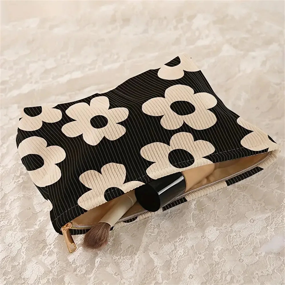 A black and white floral patterned corduroy makeup bag with a secure zipper and a brush inside.