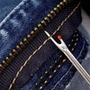 A close-up of a dark blue denim fabric showing a stitched seam with a gold thread and a stainless steel sewing needle.