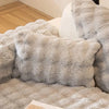 A fluffy gray decorative pillow cover is shown resting on a light-colored sofa or bed.