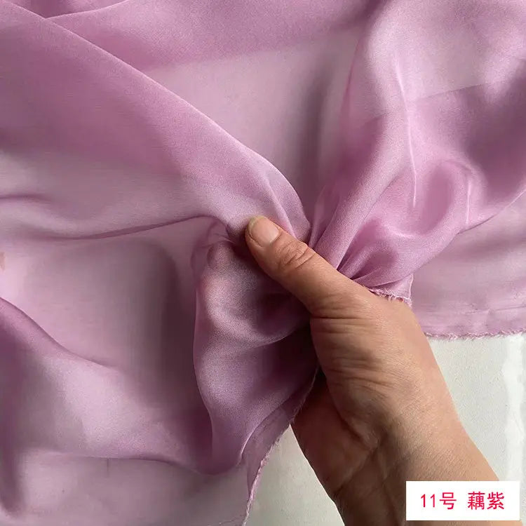 A hand is folding a piece of light purple mulberry silk chiffon fabric to show its drape and texture.