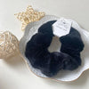 A black plush coil hair tie is displayed on a white plate next to a light beige spherical decoration.