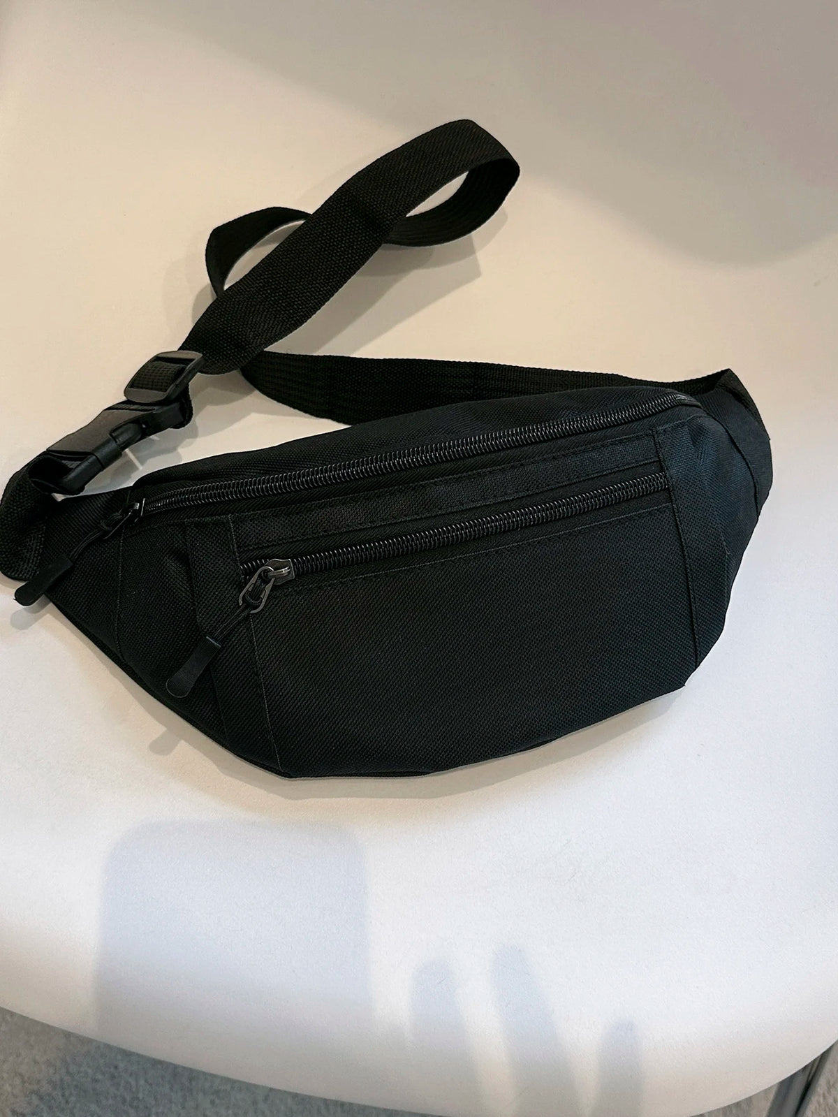 Black adjustable nylon crossbody waist pack with a strap and zipper visible on a white surface.