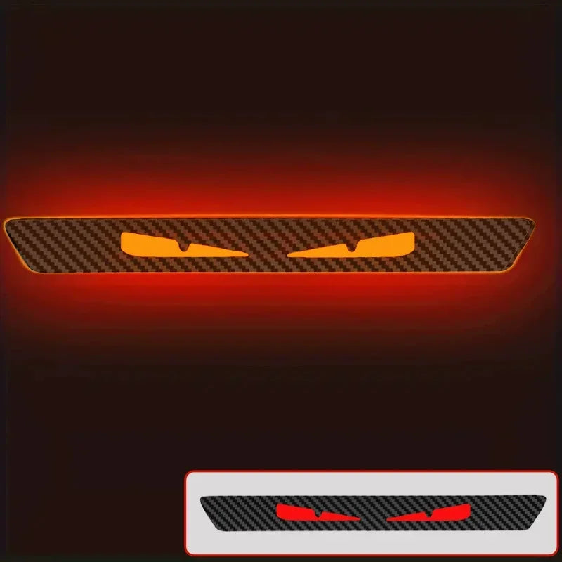 An orange devil eyes rear brake light decal on a black carbon fiber background.