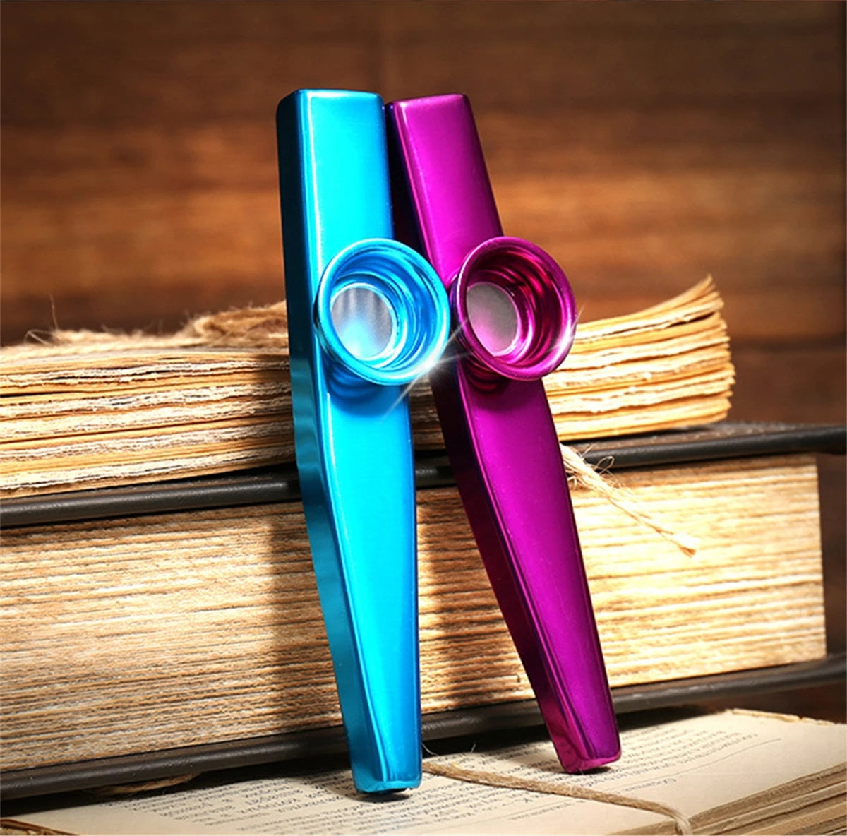 Two silver aluminum kazoo products, one blue and one purple, are displayed on a stack of books.