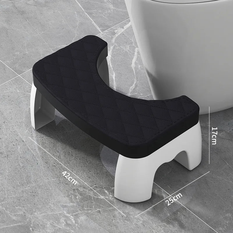 A black ergonomic non-slip toilet squat stool with white legs shown on a gray floor.