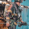 A person wearing tactical gear is holding a versatile glove and item clips for hanging.