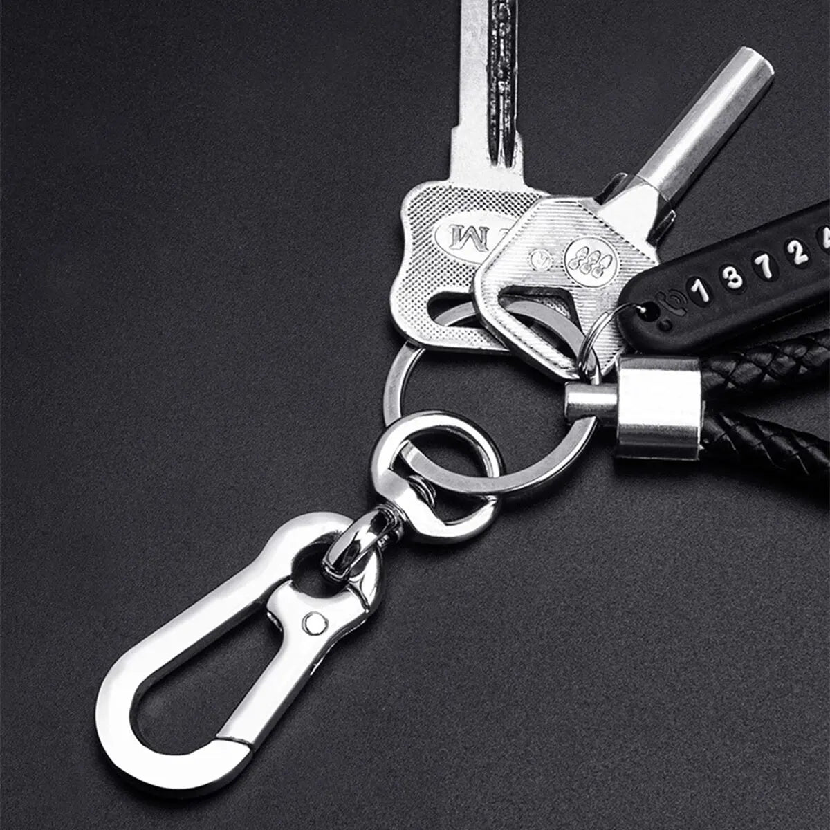 Silver keychain featuring a key, a phone number tag, and a braided black leather rope.