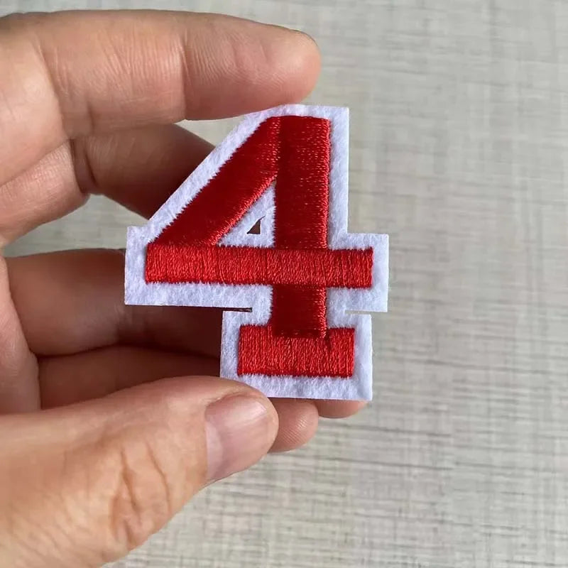 A hand holds a red iron-on 3D number patch shaped like the numeral four.