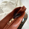 A brown leather vintage bohemian shoulder bag with golden embroidery resting on a white fabric.