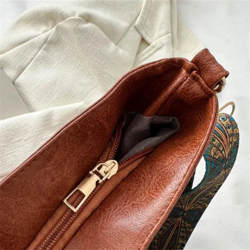 A brown leather vintage bohemian shoulder bag with golden embroidery resting on a white fabric.