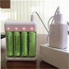 A white USB fast battery charger device with three green rechargeable batteries inserted, resting on a wooden surface.