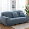 A light blue elastic stretch sofa cover for a modern couch placed in a bright room.