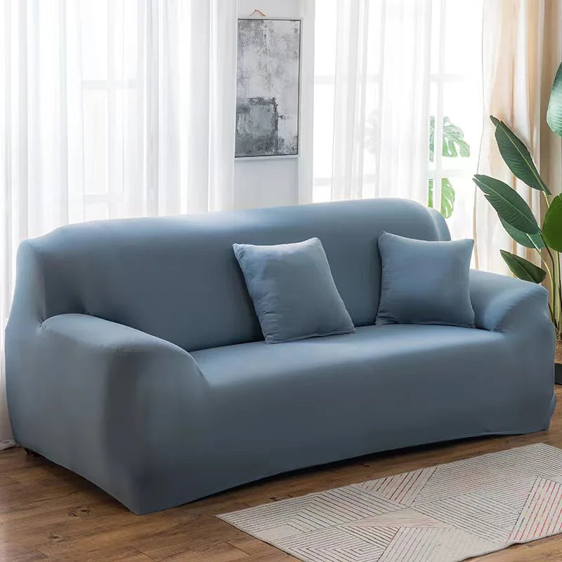 A light blue elastic stretch sofa cover for a modern couch placed in a bright room.