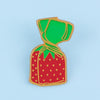 A gold-rimmed enamel pin shaped like a strawberry with a green top and a yellow-wrapped stem.