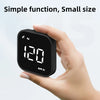 A hand holds a small black GPS head-up display device showing speed, time, and compass information.