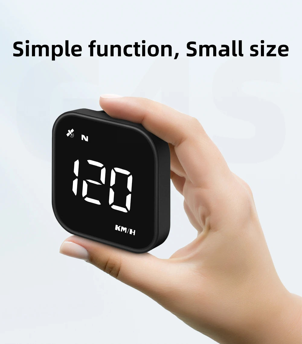 A hand holds a small black GPS head-up display device showing speed, time, and compass information.