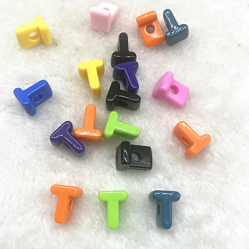 A collection of ten mixed alphabet letter beads in various colors including yellow, purple, orange, and pink, scattered on wh