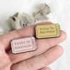 A hand holds two vintage airline ticket enamel brooches, one labeled Ticket to Anywhere and the other Ticket to Happiness.