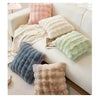 A collection of fluffy, textured decorative pillows in shades of beige, pink, and green arranged on a white sofa.