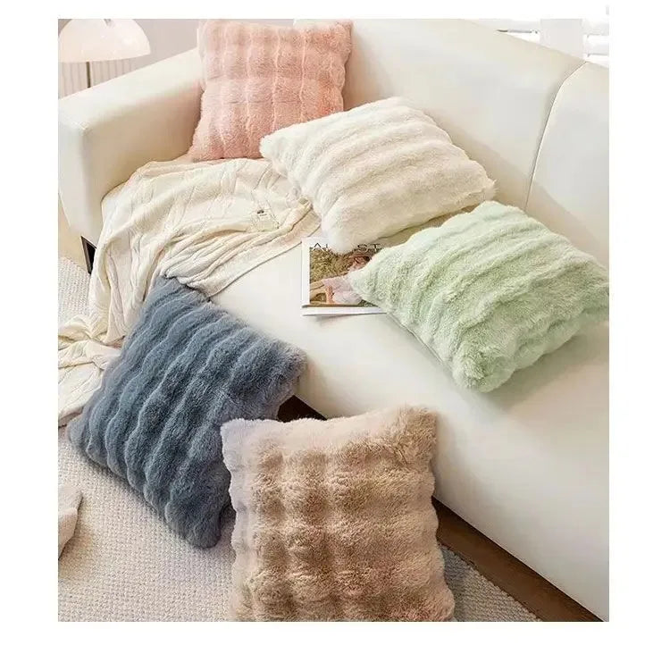 A collection of fluffy, textured decorative pillows in shades of beige, pink, and green arranged on a white sofa.