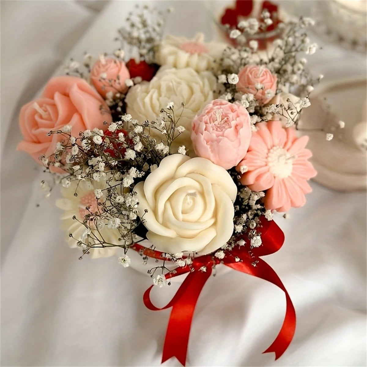 A floral arrangement of pink and cream roses and dried flowers tied with a red ribbon.