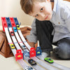 A young boy is playing with a wooden catapult racing car track set featuring various die-cast cars and sliding tracks.