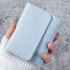 A hand holds a light blue slim triple-fold PU leather wallet against a gray background.