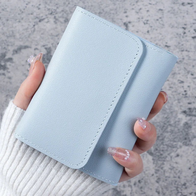 A hand holds a light blue slim triple-fold PU leather wallet against a gray background.