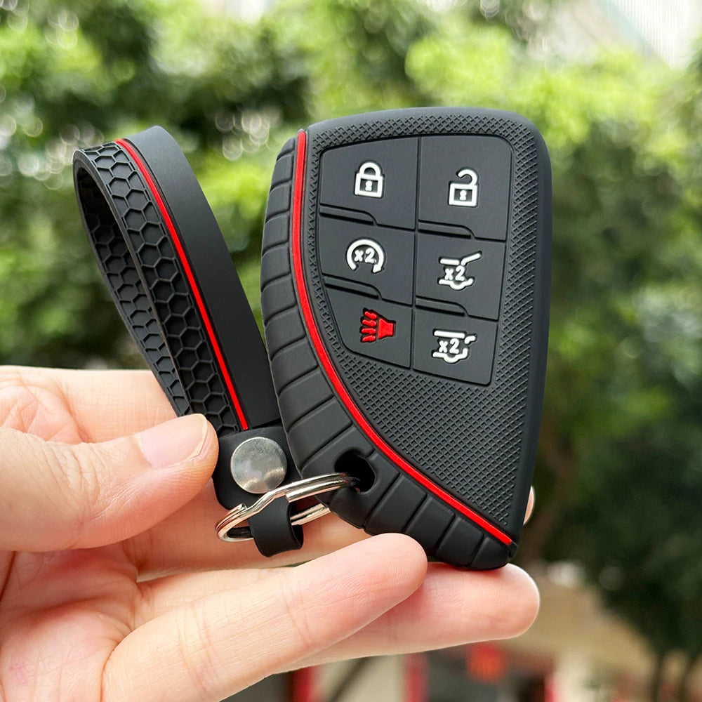 A hand holds a black silicone key fob cover with multiple buttons and a metal ring attached.